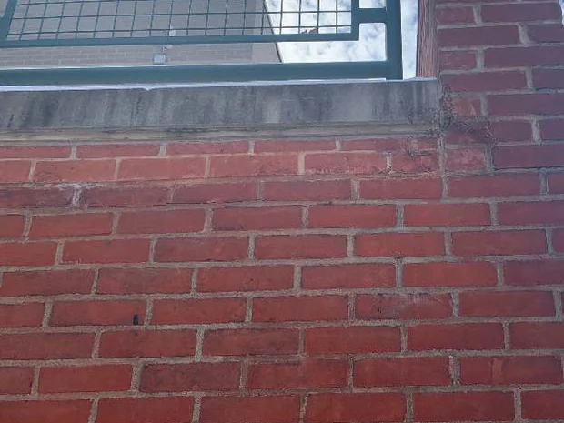 The top of the low wall in 2021 under a green railing, the former concrete band carrying brick outlines and joints that run on from the courses below it