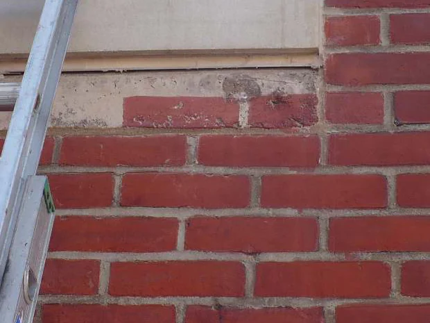 A close view of the poured concrete band in 2011 part way through staining, brick outlines and joints being worked into its surface beside an extension ladder