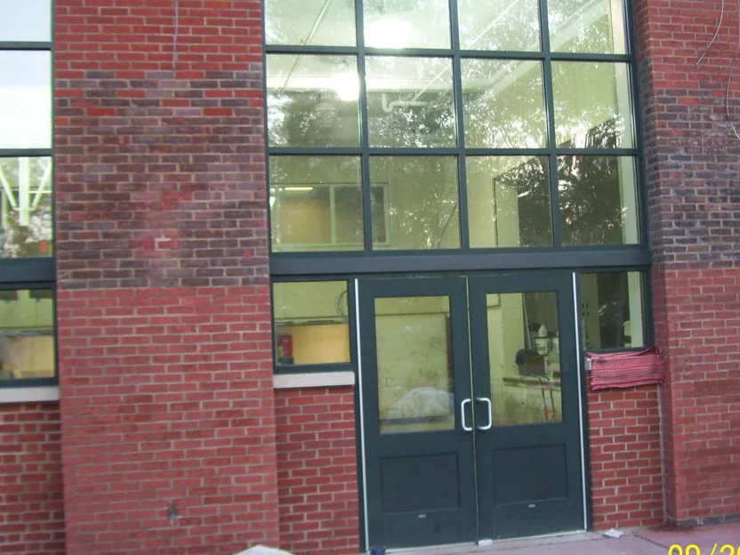 The main entrance in 2011 before staining, the two brick piers beside the double doors dark and mottled against the plain red brick of the base and the wall to the right, with a camera date stamp in the corner