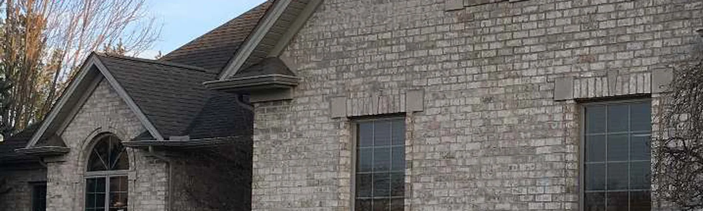 The buff brick gable wall of the Ohio house in 2019, two tall windows with cast stone headers under a shingled roof