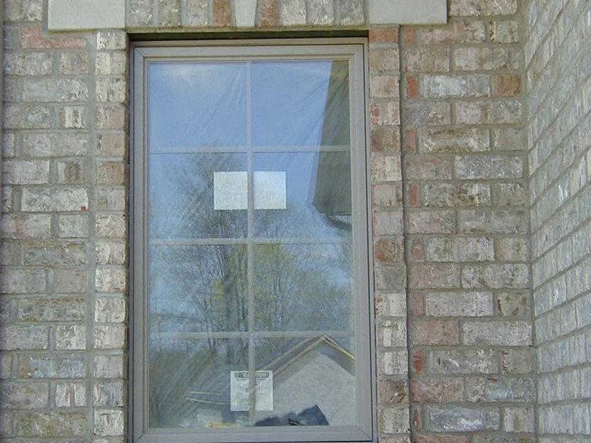 A window in 2002 framed by cast stone blocks, several cut brick in the jambs and the header reading pink and red against the buff wall around them