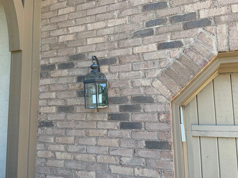 The brick at close range in 2019 behind a black carriage lantern, brown and grey units through every course with a soldier arch turning over the opening beside it