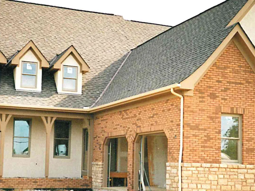 The front of the house in 1997 after staining, the brick now an even brown across the gable and the garage arches, two dormers and the covered porch to the left, the house still unfinished