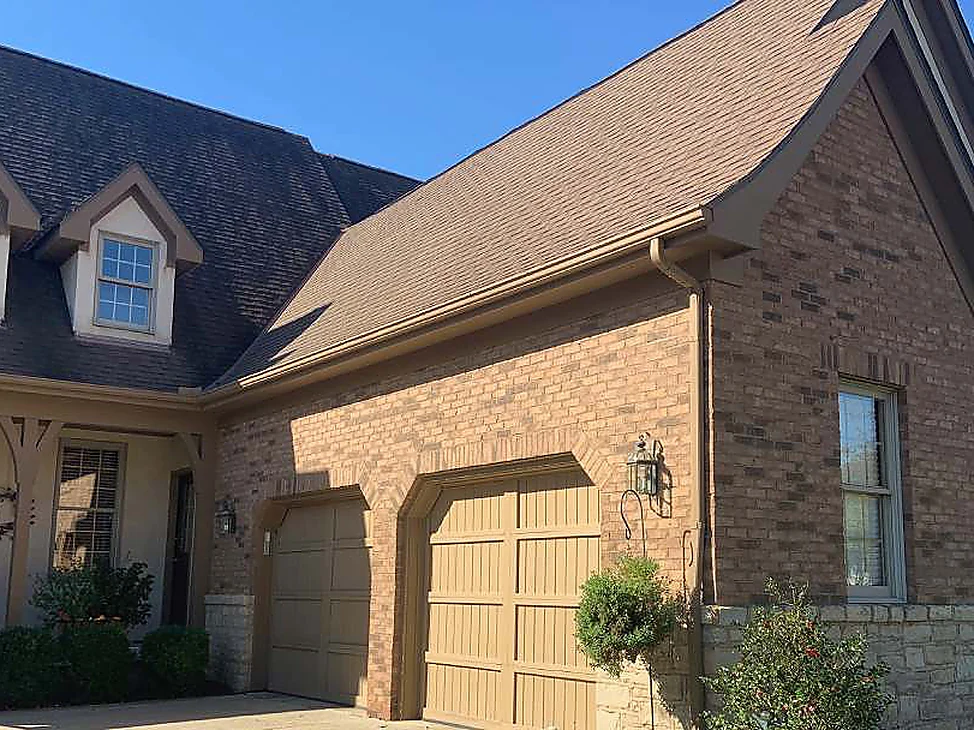 The front of the Ohio house in 2019, brown brick from the dormered roof across the gable to two arched garage heads