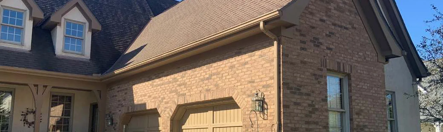 The front of the Ohio house in 2019, brown brick running from the dormered roof across the gable to the arched head of the garage