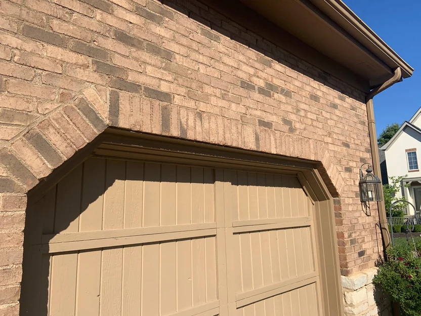 The arched head of a garage opening in 2019, brown brick set on edge turning over the door with darker units scattered through the courses above it