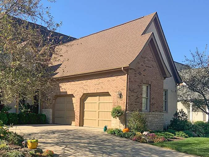 The garage wing in 2019 from the driveway, the same elevation as the 1997 frame, brown brick under a tan roof with planted beds and a brick paver walk in front