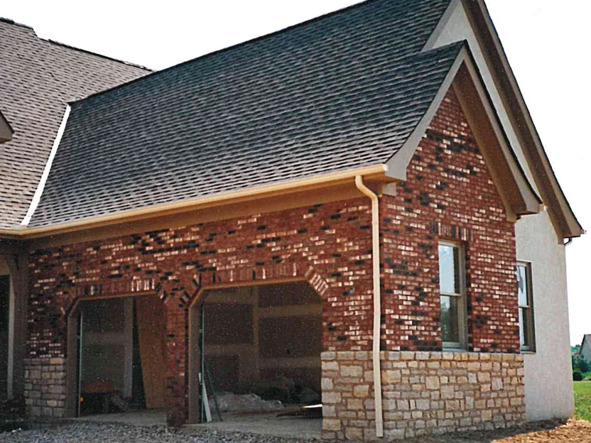 The garage wing in 1997 before staining, red brick with dark headers scattered through it meeting white brick and pale stucco, the openings still without doors and the ground bare gravel