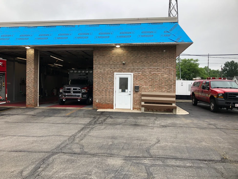 The fire station in 2019 with an apparatus bay open and an engine inside, the stained brick wall and entry door alongside it.