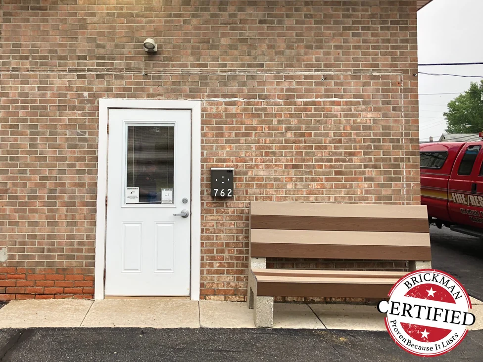 The same entry door and wall in 2019, the stained brick to the right of the door matched to its surroundings, with untouched red brick at the base on the left