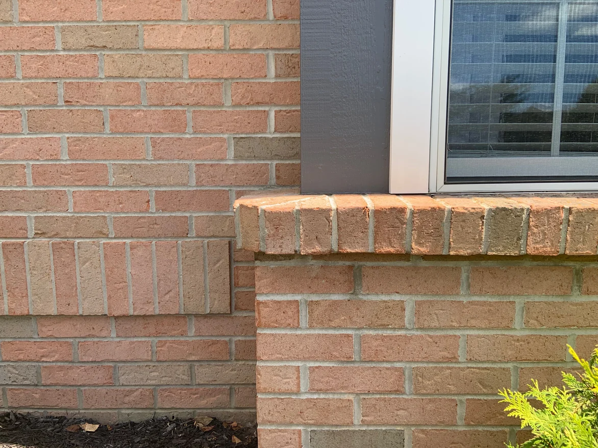Close view of the wall at a window sill in 2019, a rowlock course under the sill and the units around it an even light tan and pink range at arm's length