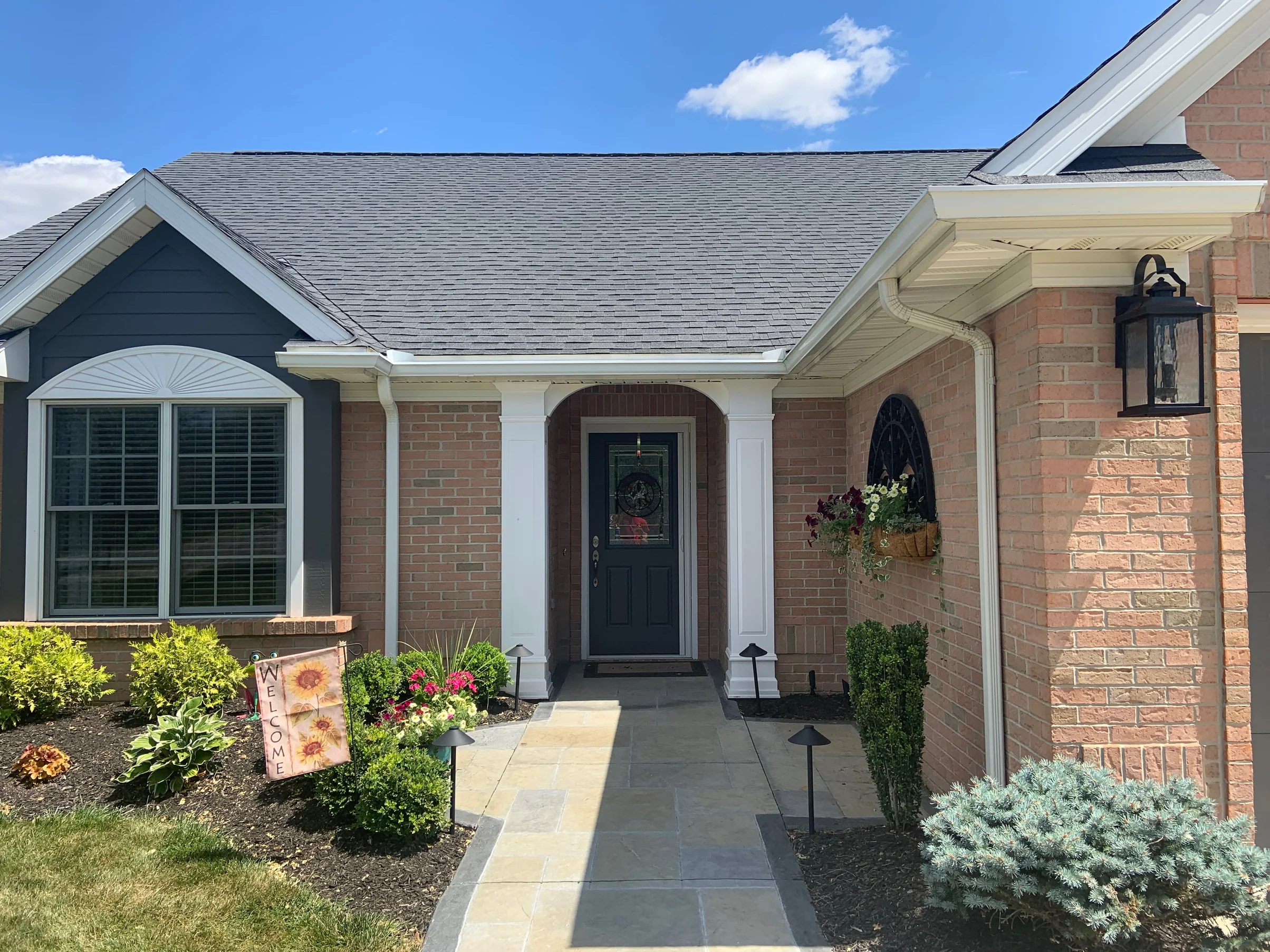 The covered entry in 2019 with a bluestone walk running up to a dark front door, brick either side of it and under the bay window in the same light range