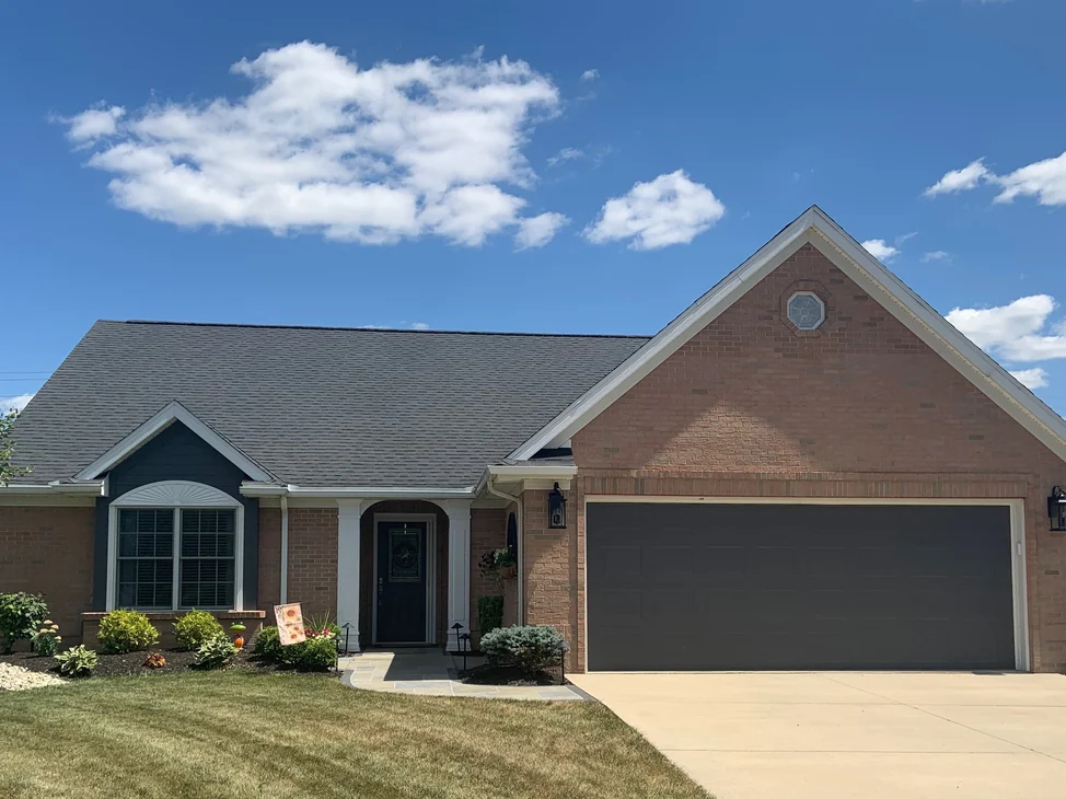 The front of the single-story house in 2019, its gabled garage wing, columned entry and bay window all in one light tan and pink brick range.