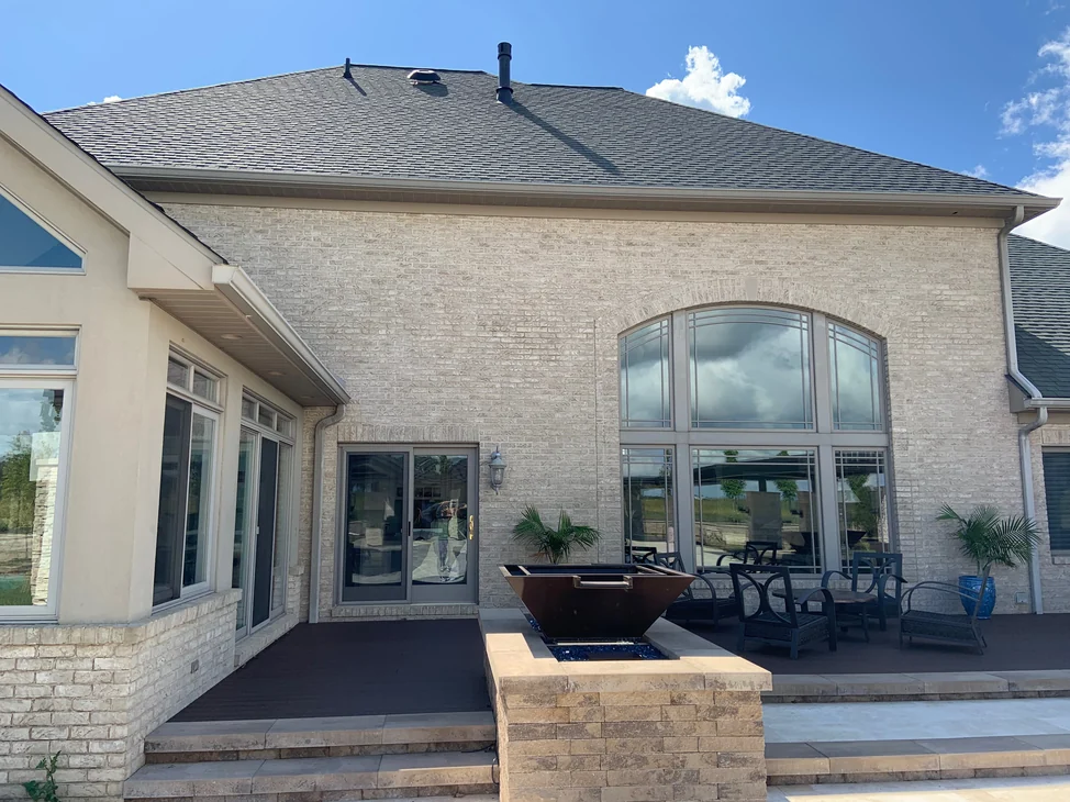 The rear of the house in 2019, a broad hipped roof over a wall of cream and tan brick with a tall arched window group above the patio.