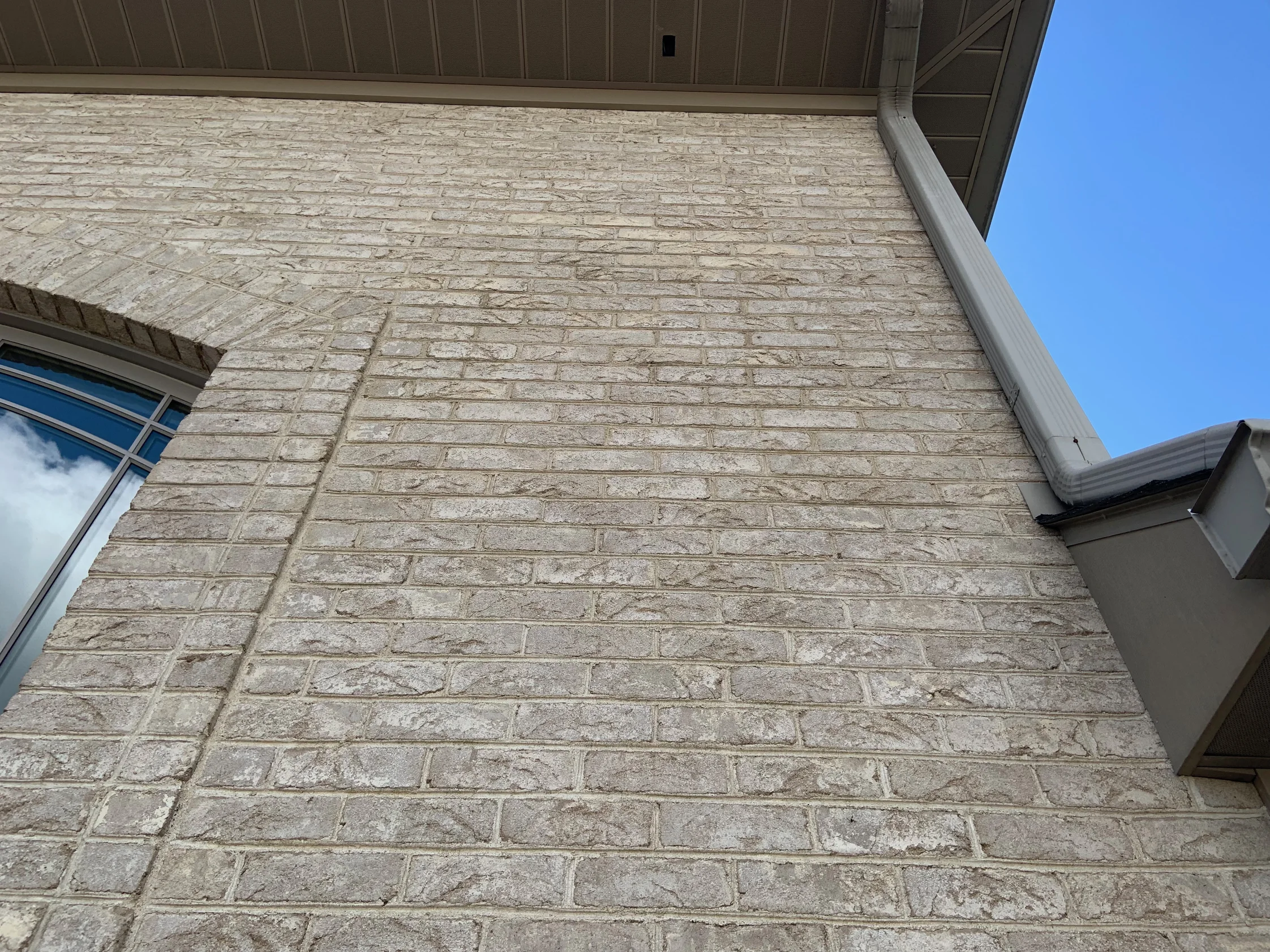 A wall of the house seen from below in 2019, the cream and tan brick running up to the eaves beside an arched window opening