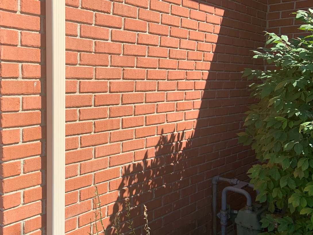 An outside corner of the house in 2019, sunlight across one face and the return wall in shadow, the brick one even red on both
