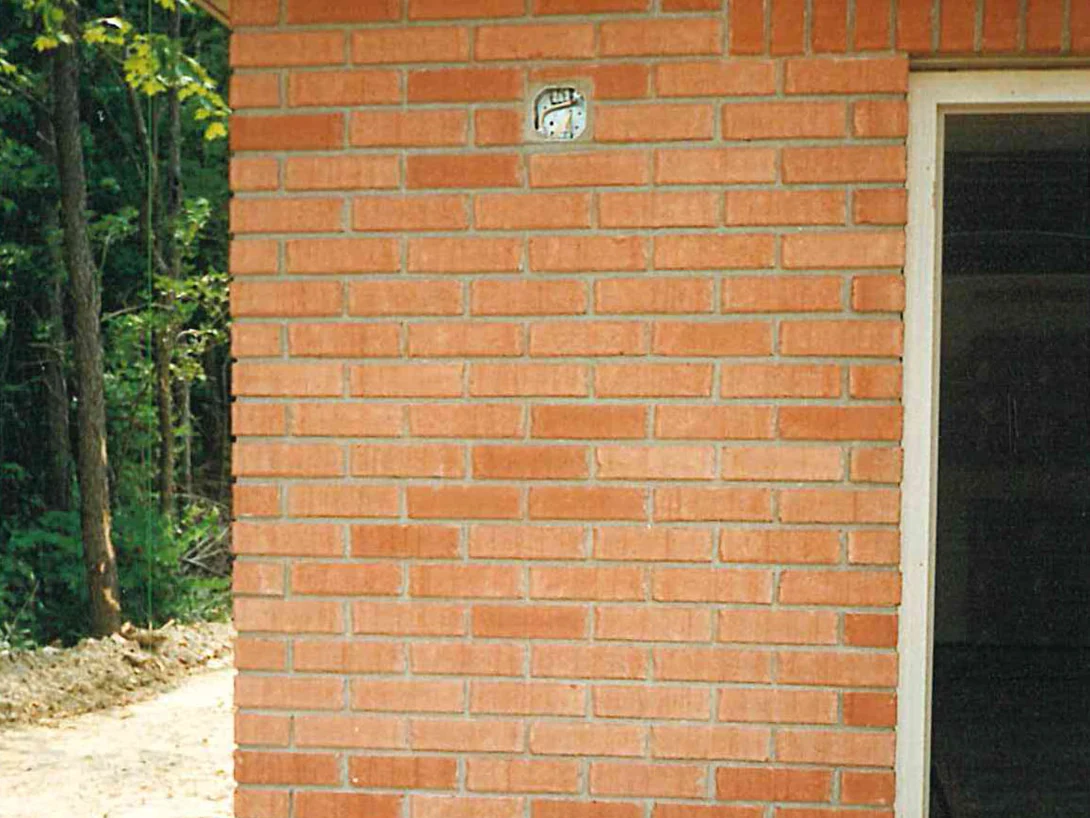 A brick wall beside an open doorway on an unfinished house in 1996, its units running from pale orange to red across the panel