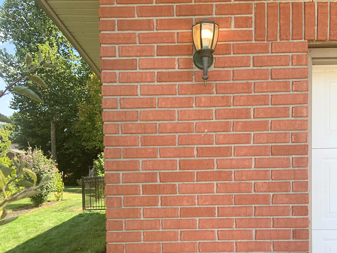 A carriage lamp on the brick beside the garage door in 2019, the units an even red from the soffit down to the flower bed