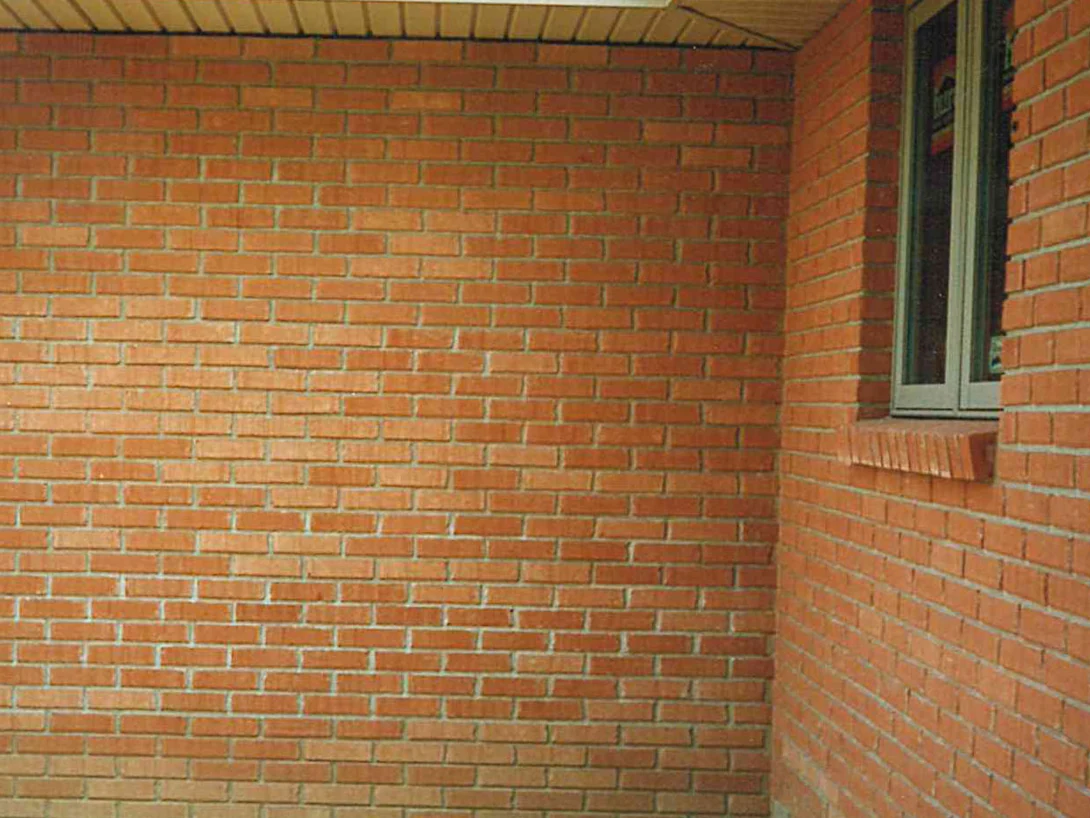 A wide brick wall under a soffit in 1996, its pale orange units meeting a darker red return wall at the corner