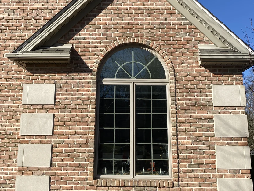 The arched window and its limestone surround in 2021, close enough to read the range unit by unit across the brick face