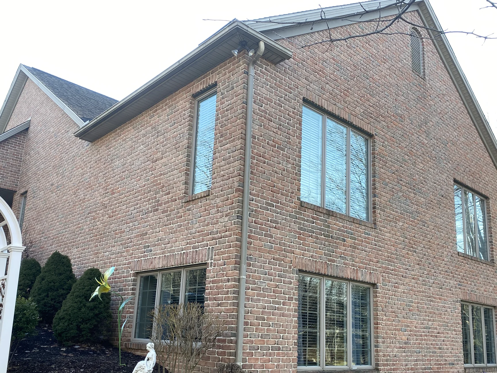 The outside corner of the house in 2021, two elevations of brick holding one even red range from the mulch beds up past two rows of windows to the gable