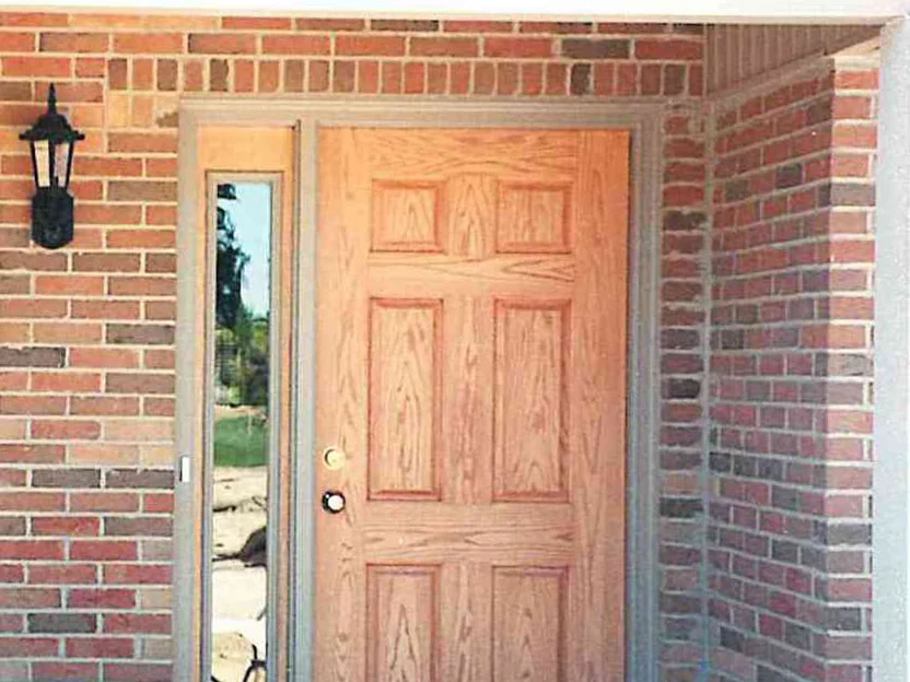 The covered front entry before the work, pale units scattered through the red and brown brick around the door and sidelight