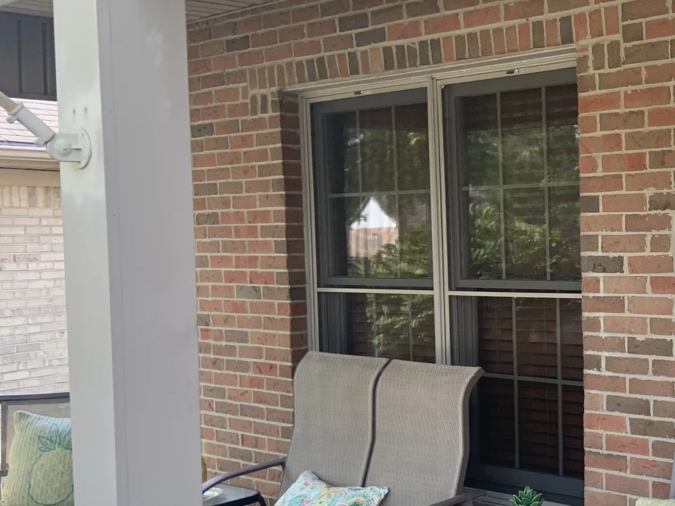 The covered porch of an Ohio house in 2019, the brick piers and the wall around the front window reading as one even red and brown range.