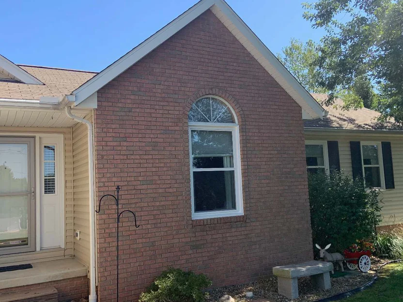 The gable and the front entry in 2019, brick running unbroken from the roof rake down past a stone bench and a gravel bed to the lawn