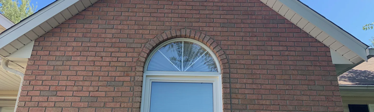 A band of the brick gable in 2019, the arched window header centred between the two roof rakes, one red and brown range through every course