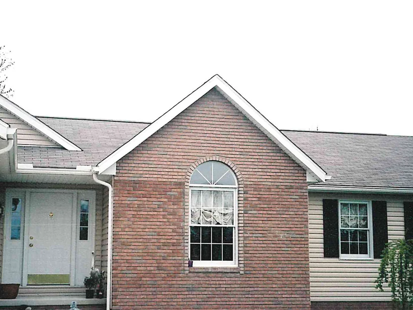 The brick gable end in 2002, pale and dark units scattered through the courses and around the arched window header, with a step stool and a ladder on the grass below