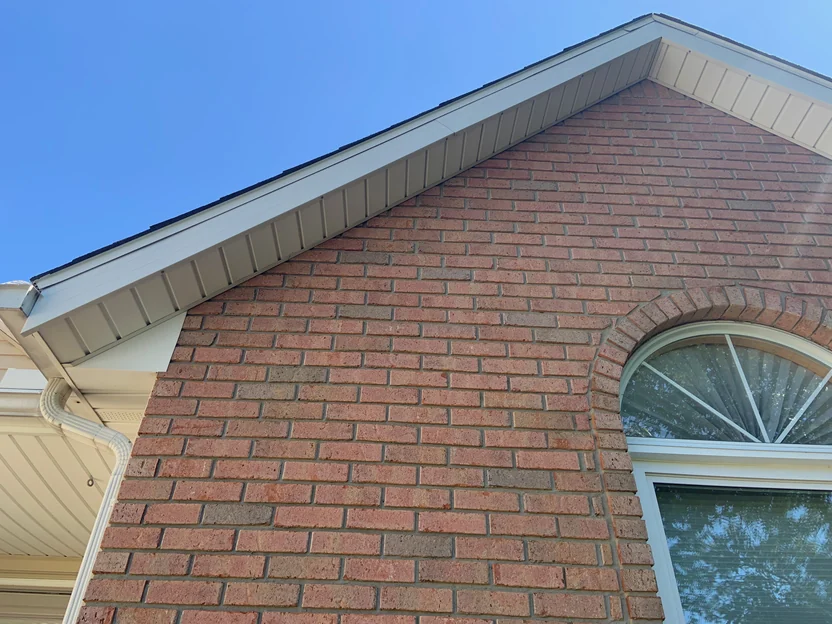 Looking up the left roof rake in 2019 at close range, brick courses running under the soffit boards to the top of the arched header at the right