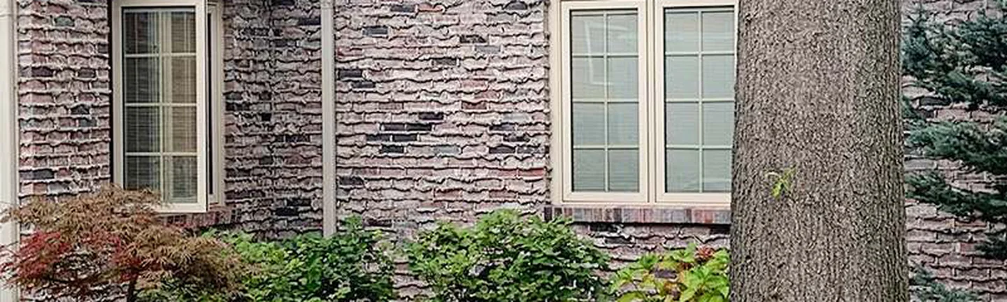 The brick wing of the Ohio house in 2019, one grey and lavender range running past two windows to a planted bed