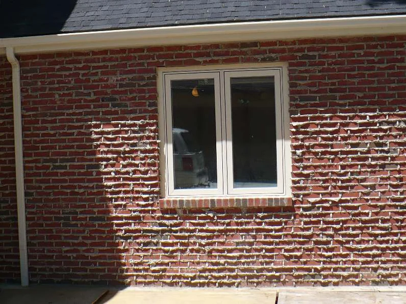 The addition wall in 2008, red brick carrying broad pale cream flashing across whole courses, a white-framed window in the middle and a downspout at the inside corner
