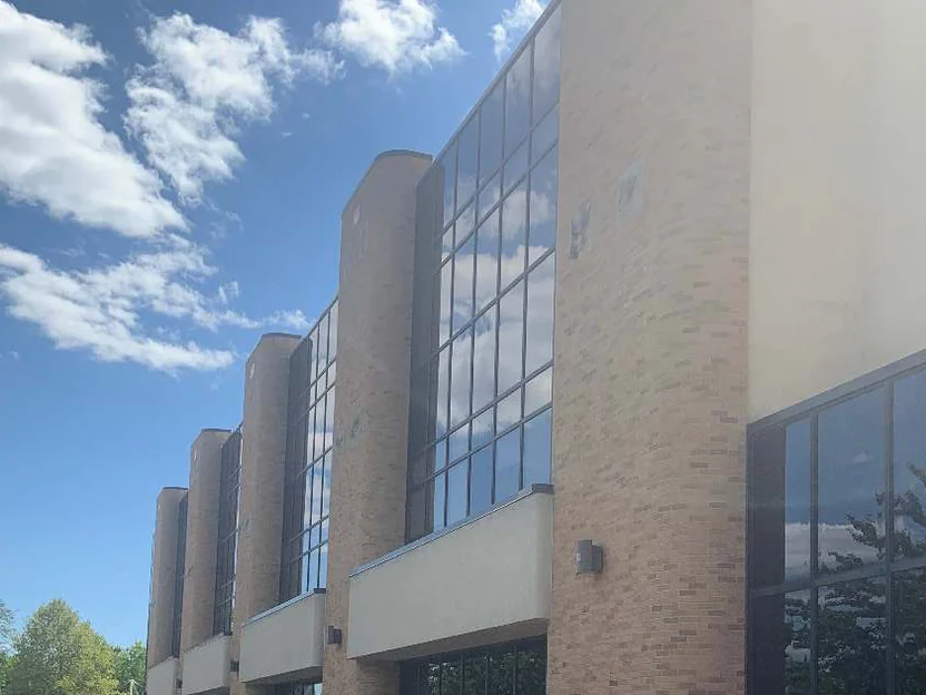 The run of rounded piers and glass bays in 2019 receding under a cloudy sky, the ground floor glazing and concrete band below