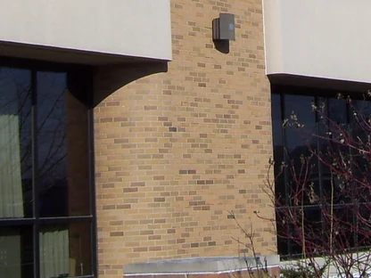 One rounded pier in 2014, buff brick with a wall lamp near the top, the concrete band and a bay of glass beside it