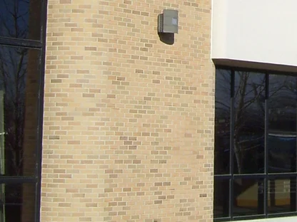 One rounded pier in 2019 with its wall lamp, buff brick reading evenly beside the concrete band and a bay of glass