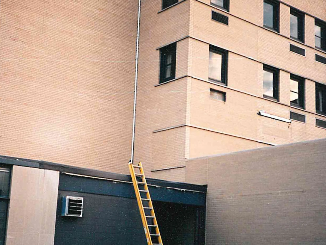 The same wall in 1997 after staining, the large panel now reading the same warm tan as the corner block beside it, the ladder still leaning on the roof