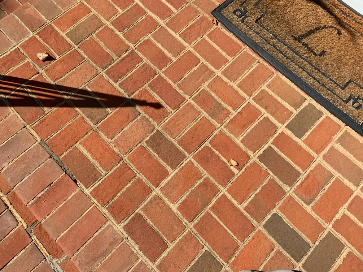 Close view of the pavers at the top landing in 2019, the units in mixed reds and browns laid in a basket weave with sand swept joints
