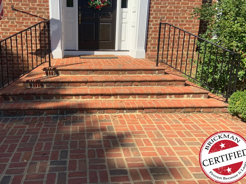 The paver steps and walk at the house entrance in 2019, treads, coping and field pavers reading as one red range, with the certification stamp at the lower right