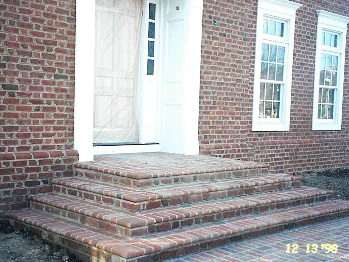 The finished paver stoop and steps at the house entrance in 1998, the treads and coping reading in the same red and brown range as the field pavers