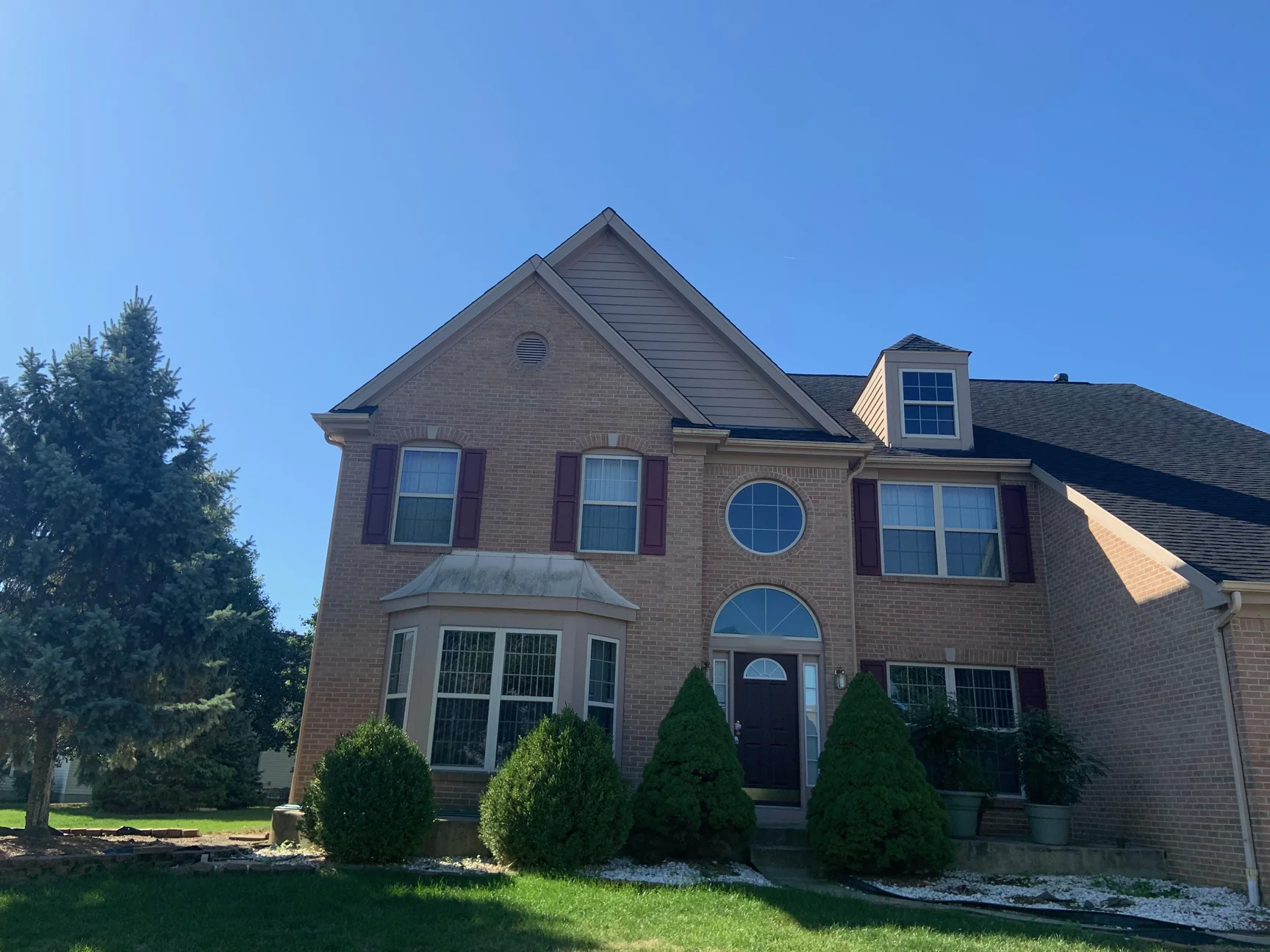The whole front of the house in 2019, the brick gable, the bay window and the arched entry holding one range of brick under a clear sky