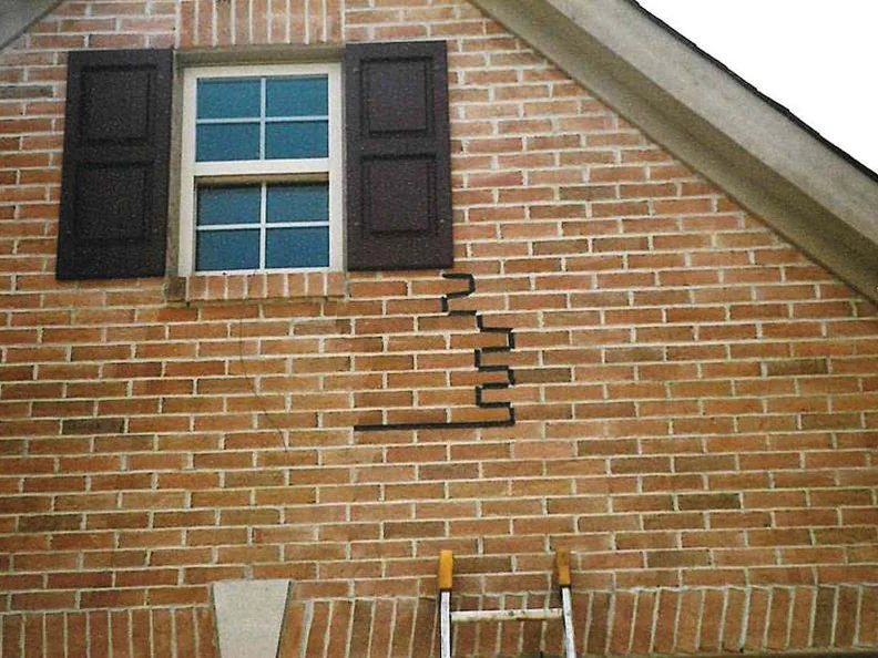 The gable wall in 2002, a marked line stepping down through the courses beside the shuttered window, pale washed brick on one side of it and fuller red brick on the other, with a ladder standing below