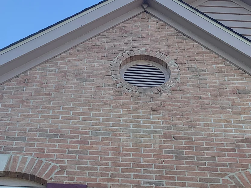 The front gable in 2019, a round louvred vent ringed with brick, the courses around it holding one color out to the eaves