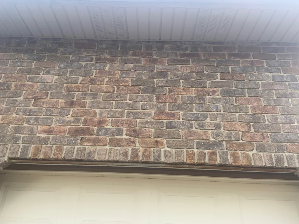 Close view of the brick above a garage opening, the oversized units running through red, brown and near black over pale mortar joints