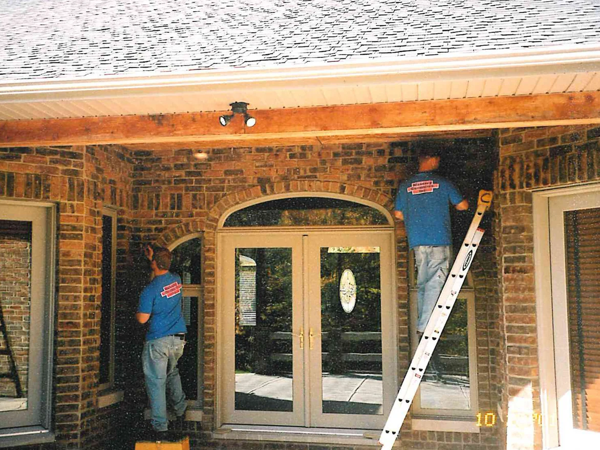 Two applicators in Masonry Cosmetics shirts working the brick of a covered entry, one standing on a step stool and one on a ladder beside the arched double doors