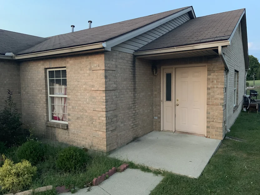 A side entrance under a shallow gabled porch in 2019, the brick returning around the outside corner in the same range