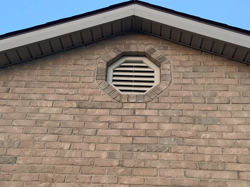The garage gable in 2019, an octagonal louvred vent set into a brick surround with the field evenly ranged either side of it
