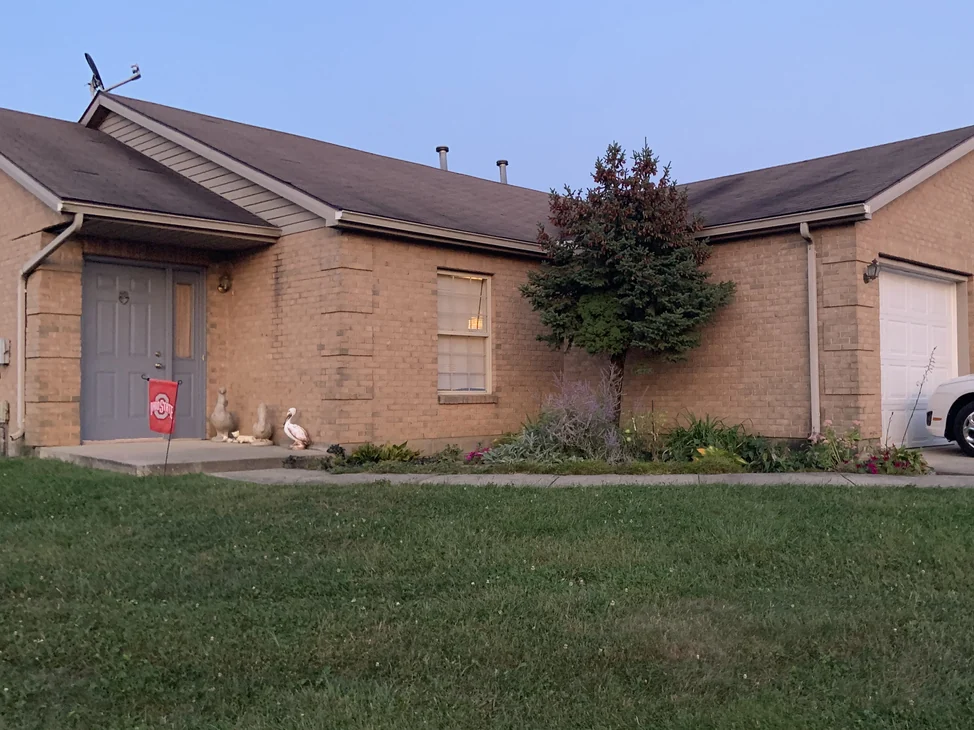 The house seen from across the front lawn in 2019, the entry, the window bay and the garage wing all in one tan brick range.
