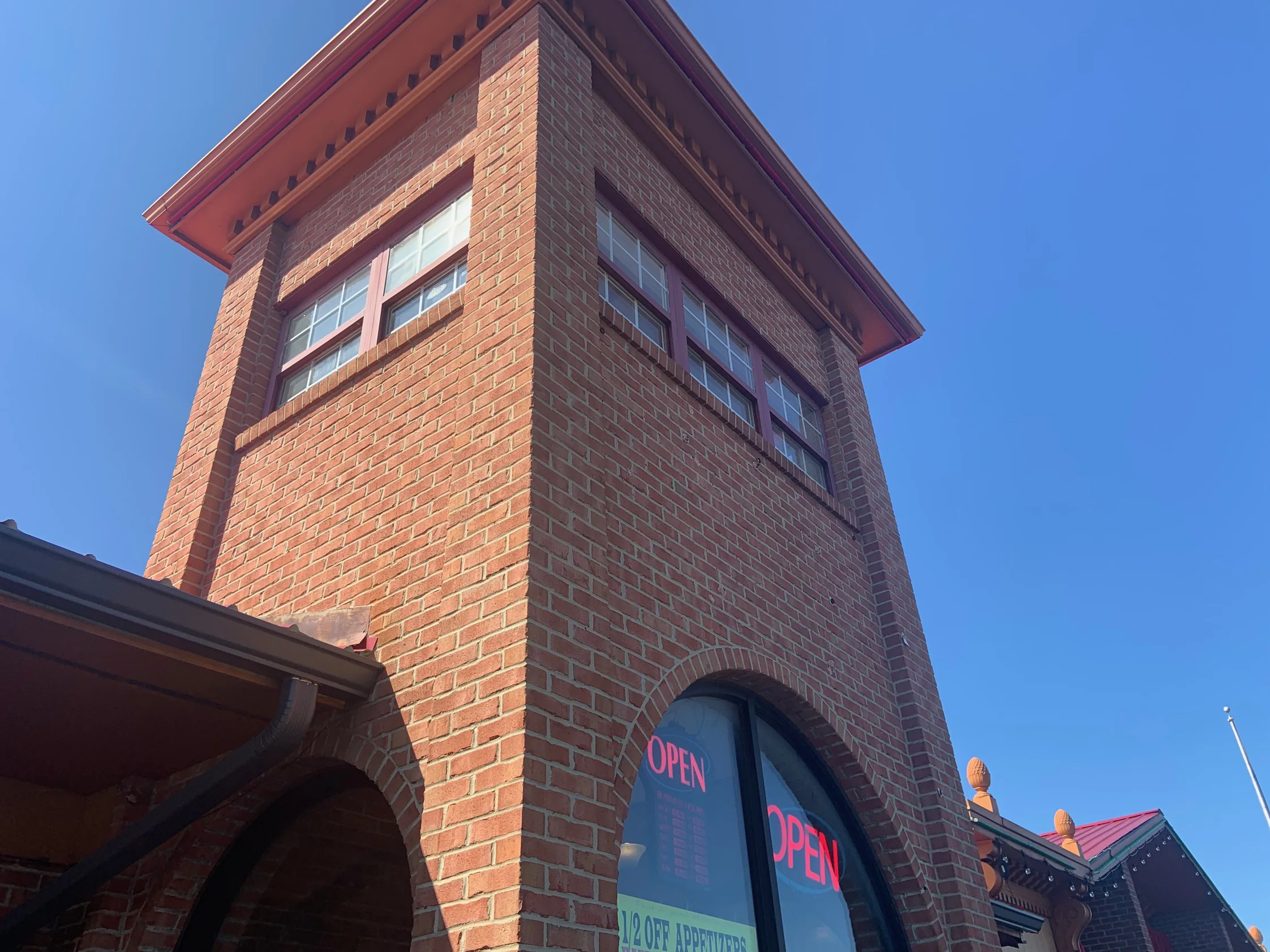 The entry tower from the pavement in 2019, two faces of red brick meeting at the corner under a projecting cornice against a clear sky