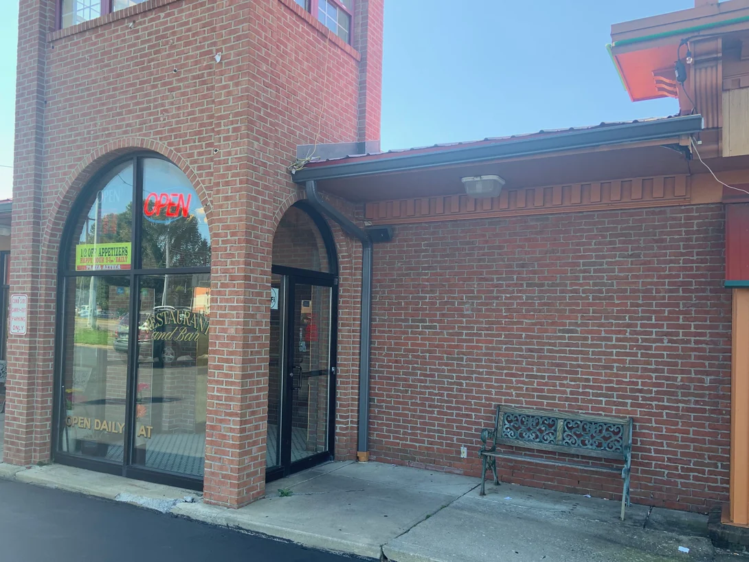 The restaurant entrance in 2019, an arched display window and a recessed door set in brick that reads as one red range along the wall